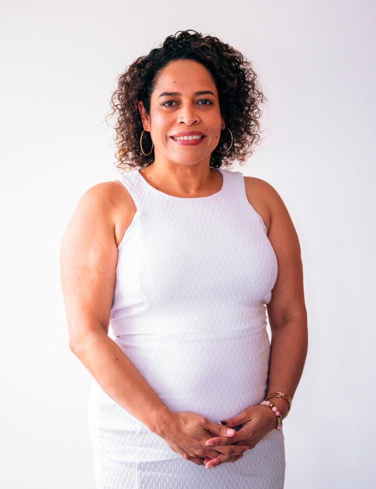 woman with dark brown curly hair wearing a white sleeveless pique dress